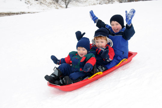Three young boys sledding downhill together