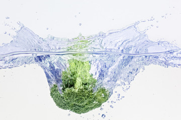 Green broccoli falling in water with air bubbles