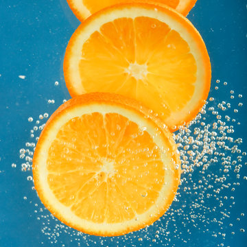 Fresh orange dropped into water with bubbles.