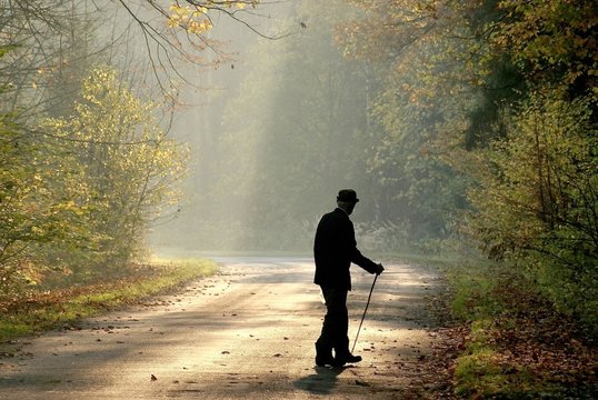 Fototapeta Older man through the country road in autumn forest