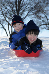 Two young boys sledding downhill together