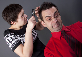 Woman examining man's hair with magnifying glass