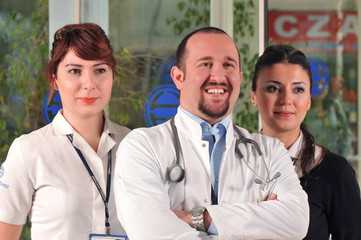 A medical doctor and two nurses smiling at hospital entrance