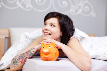 fröhliche junge frau mit sparschwein im bett