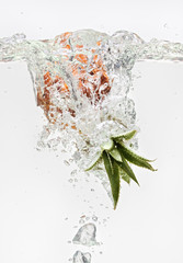 Small pineapple falling in water on white