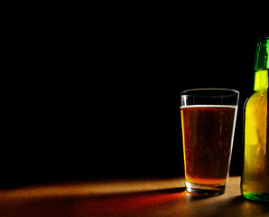 pint glass of beer and bottle, on black background