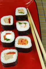 sushi futomaki on red plate with chopsticks