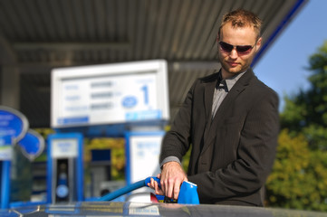 Junger Mann im Anzug tankt sein Auto auf