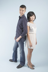 A young Asian couple standing together back to back and smiling