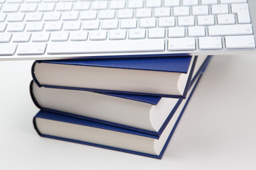 Stapel B&uuml;cher vor wei&szlig;em Hintergrund, mit Computertastatur