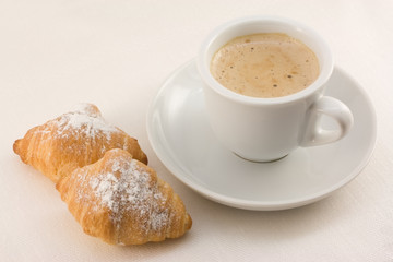 Cup of coffee with two croissants on a white linen cloth