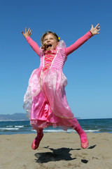 Girl dressed as a princess jumps into the air on a beach