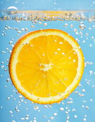 Fresh orange dropped into water with bubbles.