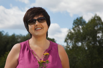 woman in sunny day on wood clearing smiles and holds flowers