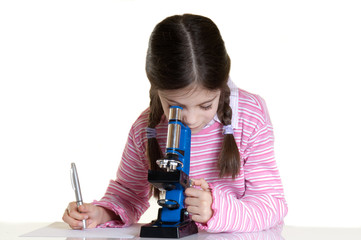 little girl writing  and looking with microscope in school