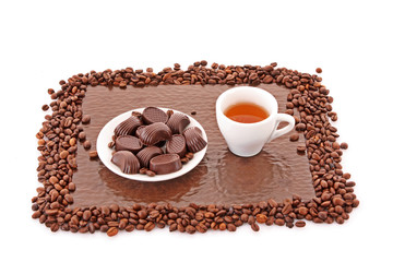 Assorted chocolate candies and cup of tea on brown background