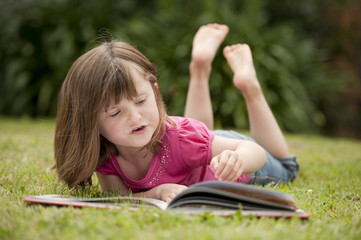 little girl laying in grass reading