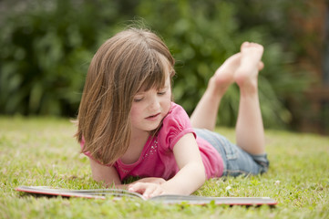 little girl laying in grass reading