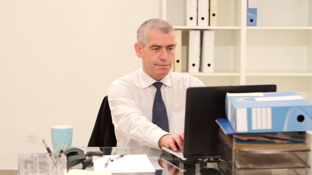Mature businessman sitting at desk in office with laptop