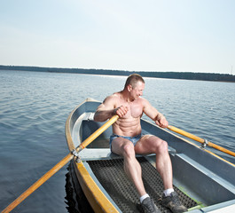 Muscular man with oars in boat