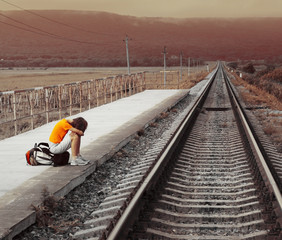 Naklejka premium Young sad woman with a backpack waiting for a train at the station
