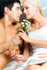 Young happy amorous couple with champagne at bedroom