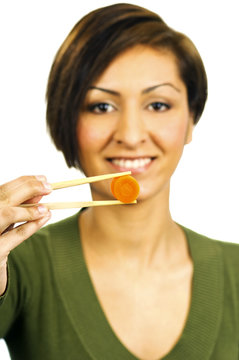 Young woman holds a carrot slice with chopsticks in front of her