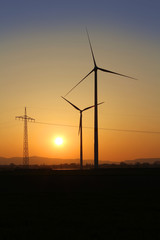 Windrad und Strommast im Sonnenuntergang