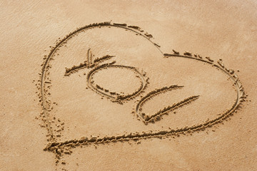 Heart shape symbol with the word you on sandy beach