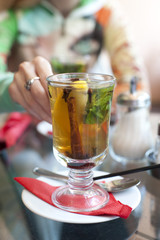woman taking a glass of tea with lemon, cinnamon stick, mint