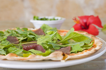 Meat pizza on a thin base with green salad topping