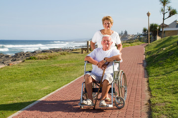 kind senior wife pushing happy husband in wheelchair