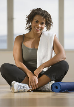 African woman sitting next to yoga mat