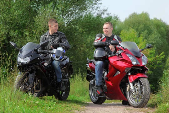 two motorcyclists standing on country road, without helmets