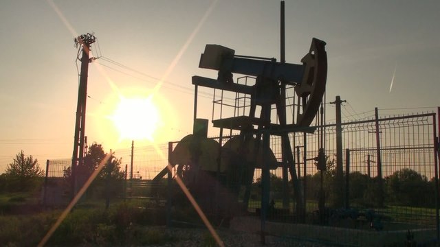 An oil pump jack in action at sunset – backlight
