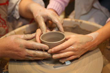 Hands of people create pot on potter's wheel.