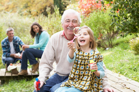 Grandfather And Granddaughter Blowing Bubbles On Family Picnic
