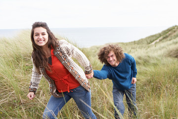 Naklejka na ściany i meble Young Couple Walking Through Sand Dunes Wearing Warm Clothing