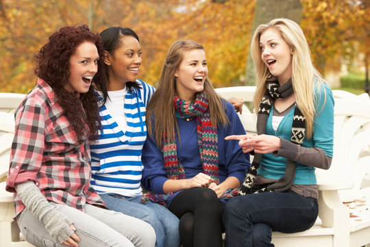 Group Of Four Teenage Girls Sitting On Bench In Autumn Park