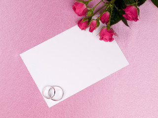 Silver wedding rings, card  and roses on a pink background