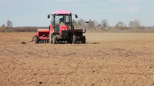 Red tractor seeding grain in early spring