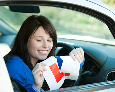 Brunette teen girl sitting in her car tearing a L-sign