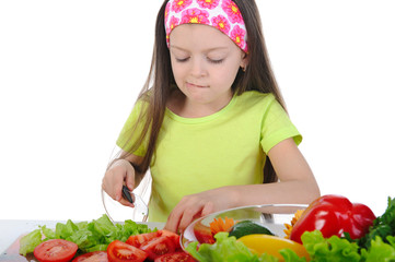 Little girl cut tomatoes at the table
