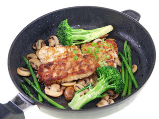 fried fish with vegetables in a black pan isolated on white