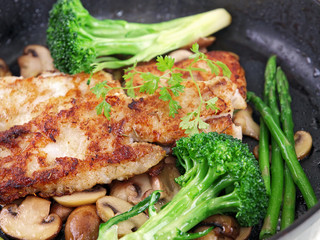fried breaded fish with vegetables in a black pan