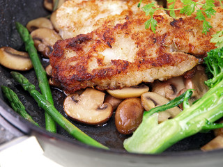 fried fish with vegetables in a black pan isolated on white