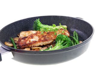 fried fish with vegetables in a black pan isolated on white