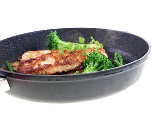 fried fish with vegetables in a black pan isolated on white