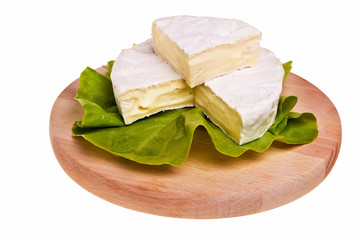 Round camembert cheese on lettuce on cutting board.