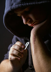 Hooded man holding a razorblade to the scar on his arm - 22533940